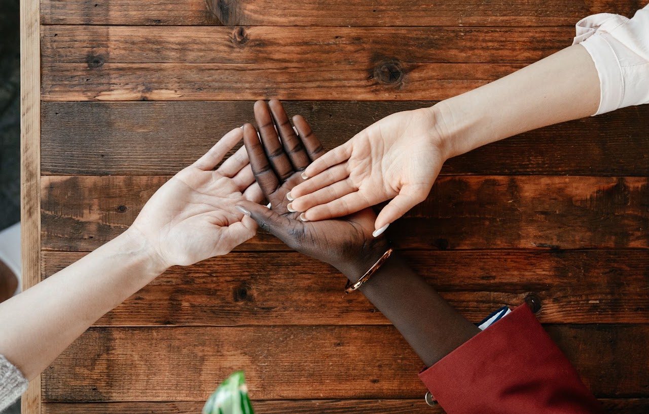 Plusieurs mains réunies au-dessus d'une table en bois, geste de solidarité